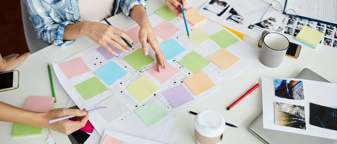 People sitting around desk with post-it notes near notes and mugs to plan silent auction