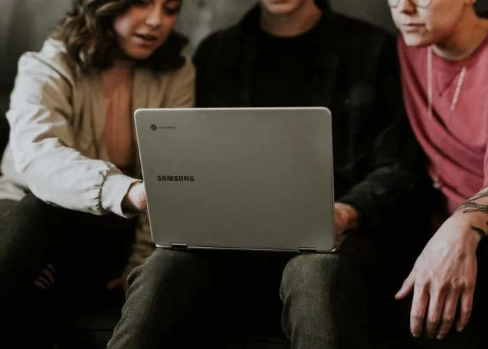 Three people browse through online silent auction items on a computer, selecting which to bid on.